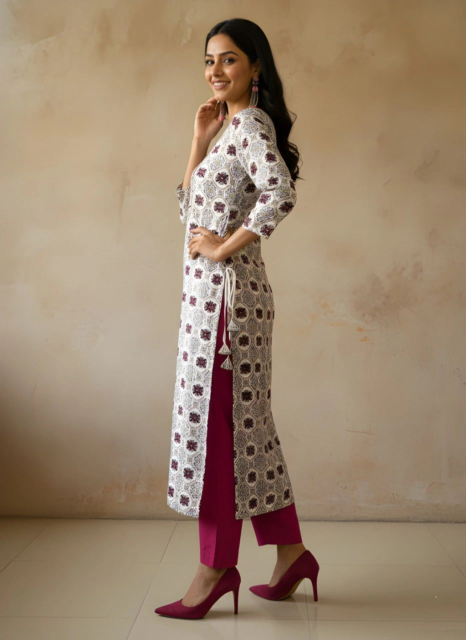 Woman wearing a long, patterned white dress with maroon accents against a beige background
